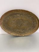 A large Syrian brass oval scalloped tray, the centre panel with stylised winged God and Syrian style