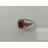 A 9ct gold ring with an oval cut red/orange stone, flanked by diamonds above and below, one