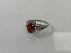 A 9ct gold ring with an oval cut red/orange stone, flanked by diamonds above and below, one