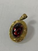 A yellow metal set oval cabuchon garnet pendant / brooch, mounted in an oval engraved frame, (2.