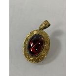 A yellow metal set oval cabuchon garnet pendant / brooch, mounted in an oval engraved frame, (2.