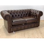 A Chesterfield two seat sofa, upholstered in deep buttoned brown leather, with two squab cushions,