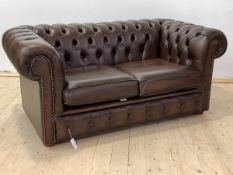 A Chesterfield two seat sofa, upholstered in deep buttoned brown leather, with two squab cushions,