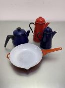 A blue enamelled teapot, a blue enamelled hot water jug, a larger red enamelled coffee pot, and a