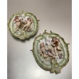 A pair of continental porcelain oval relief cast panels depicting winged cherubs with busts, in