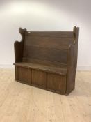 An early 20th century oak settle, the seat, back and three panel front enclosed by panel end