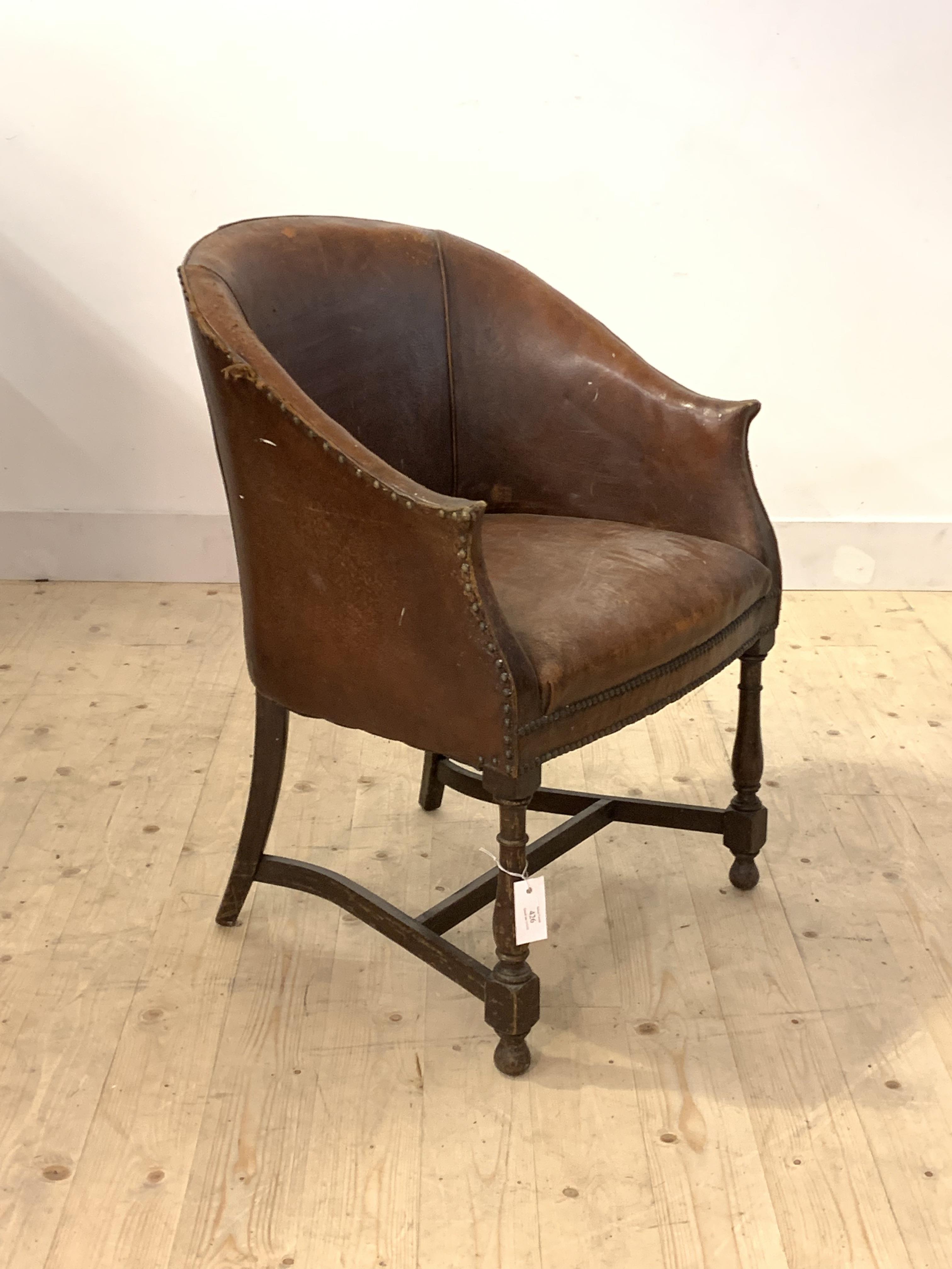 An early 20th century leather upholstered tub chair, raised on turned supports united by stretchers,