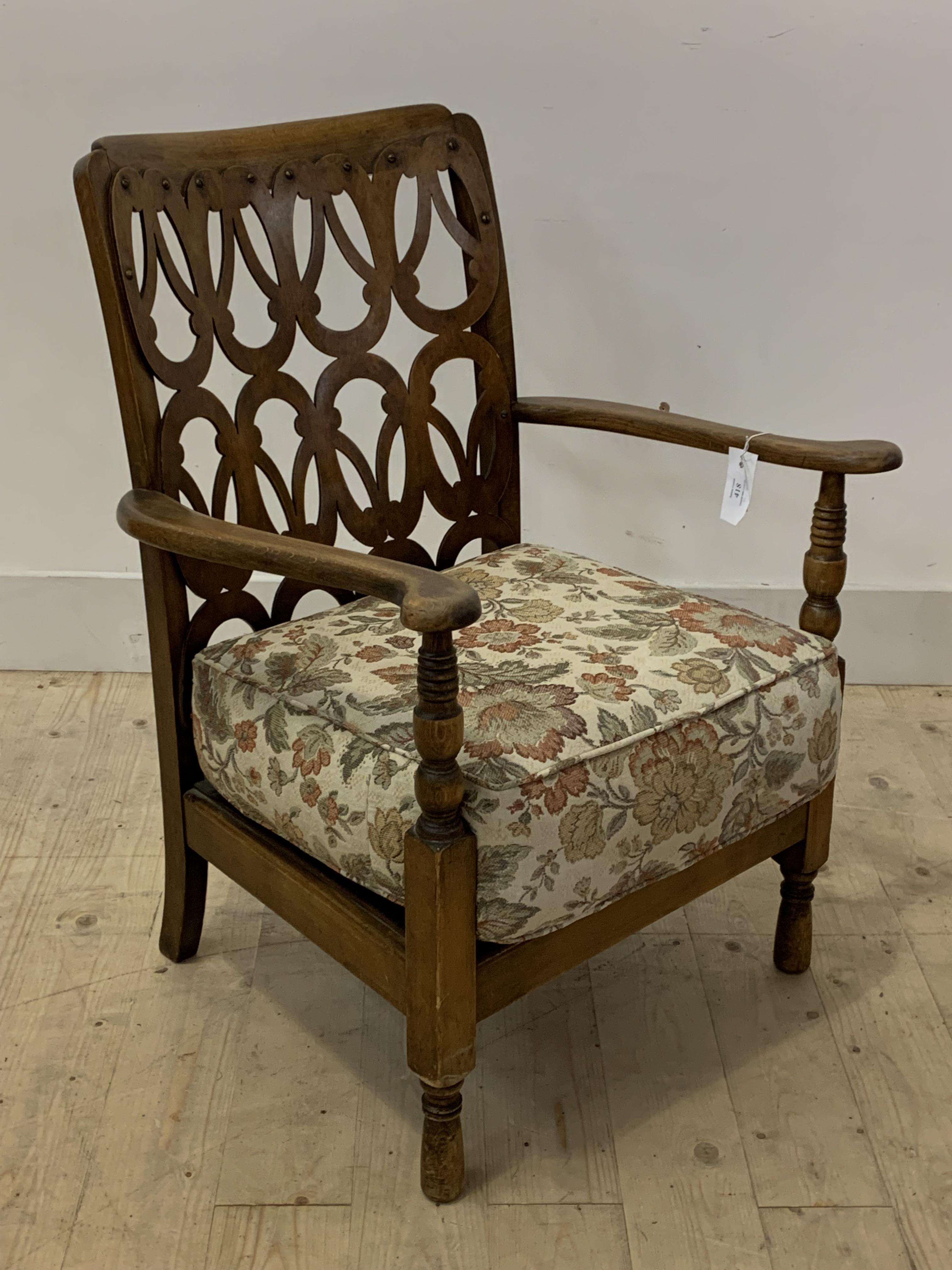 An early 20th century stained beech open armchair, with an unusual fret carved back panel over squab