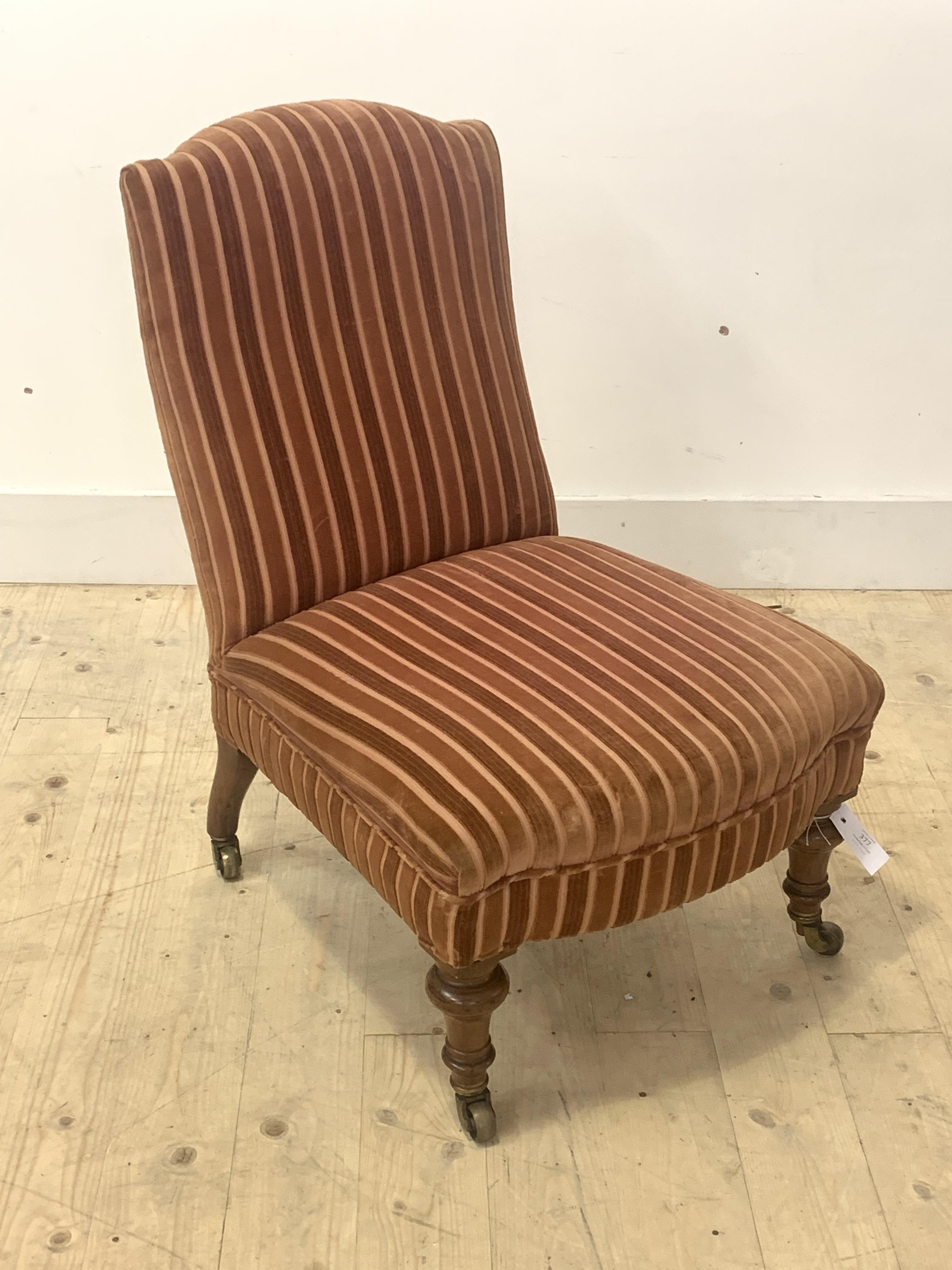 A Victorian slipper chair, upholstered, raised on turned walnut supports terminating in brass