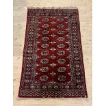 A hand knotted bokhara rug, the red field with two rows of guls and bordered, 96cm x 162cm