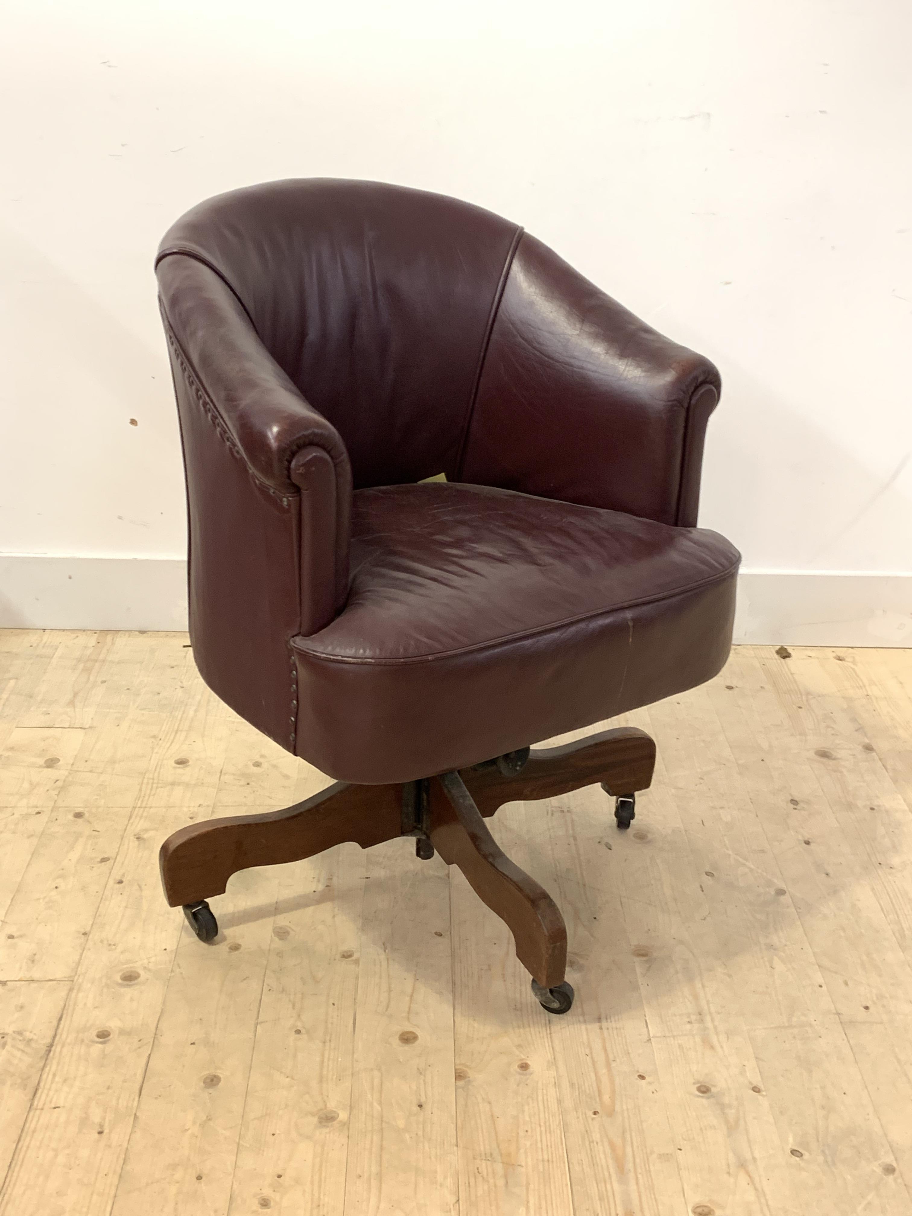 An early 20th century leather upholstered tub shaped desk chair, reclining and on a swivel base with