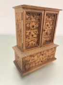 A late 19thc treen carved miniature cabinet bookcase with a pair of panelled doors, missing glass,