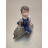 A Royal Copenhagen Danish porcelain figure of a boy on a marrow decorated with polychrome enamels (
