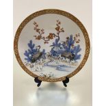 A Japanese late 19thc porcelain plaque decorated with cranes and prunus by a stream, enclosed within