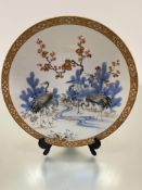 A Japanese late 19thc porcelain plaque decorated with cranes and prunus by a stream, enclosed within