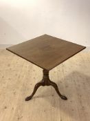 A George III mahogany tilt top table, the square top over ring turned column and triple splay