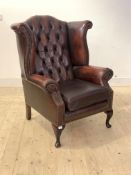 A Georgian style wingback chair, upholstered in deep buttoned oxblood leather, raised on cabriole