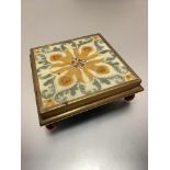 An Edwardian Minton style daffodil and leaf pattern tile mounted in brass frame on ball feet, used
