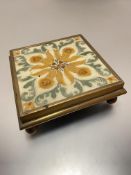 An Edwardian Minton style daffodil and leaf pattern tile mounted in brass frame on ball feet, used