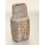 A hand-thrown pottery coffin style vase with vertical lines to top and impressed symbol to centre