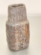 A hand-thrown pottery coffin style vase with vertical lines to top and impressed symbol to centre