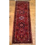 A Persian hand knotted runner rug, the busy red field with floral pole medallion, 109cm x 327cm