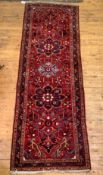 A Persian hand knotted runner rug, the busy red field with floral pole medallion, 109cm x 327cm