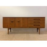A mid century teak sideboard, the concave front with two cupboard doors and three drawers, raised on