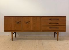 A mid century teak sideboard, the concave front with two cupboard doors and three drawers, raised on
