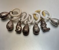 A collection of seven white metal chased child's rattles with composition teething rings, some in