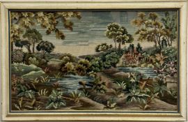 An embroidered gros point panel depicting cottage by a lake with trees shrubs and plants in gilt