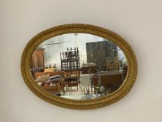 An Edwardian gilt composition framed oval wall mirror, the frame with egg and dart, fluting and