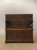 An early 20th century carved oak monks bench, the folding back over hinged seat and three panel