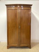 An Edwardian mahogany bow front wardrobe, the projecting cornice over two panelled doors enclosing a