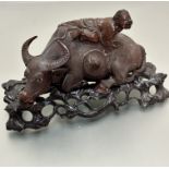 A carved Chinese hardwood water buffalo figure with boy crawling across his back, with inset glass