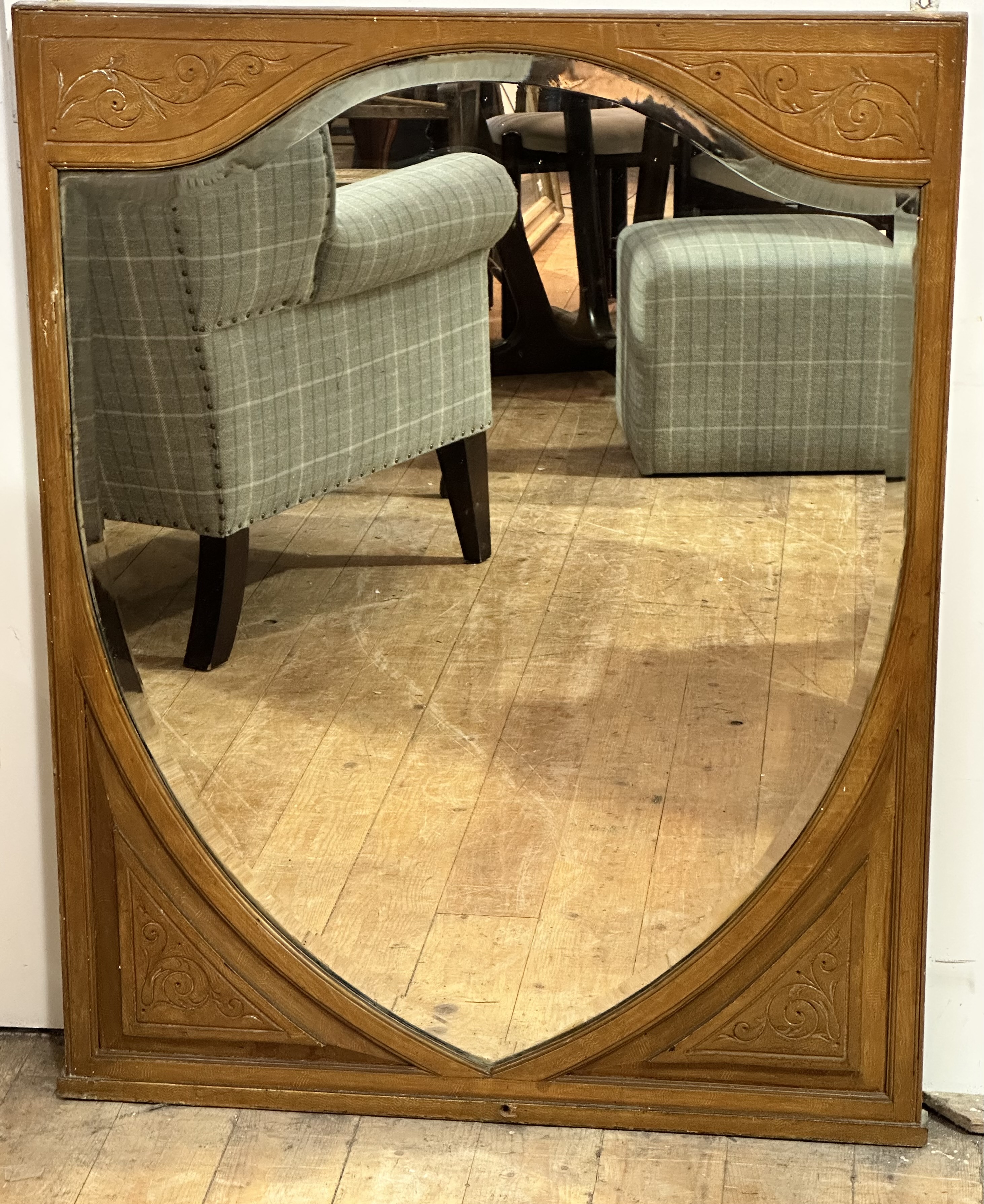 An Edwardian stippled oak frame and carved shield shaped mirror with relief carved panels,