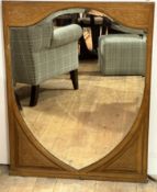 An Edwardian stippled oak frame and carved shield shaped mirror with relief carved panels,