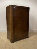 A 1920s figured walnut gentlemans compactum, with two doors enclosing a hanging rail and shelves, on