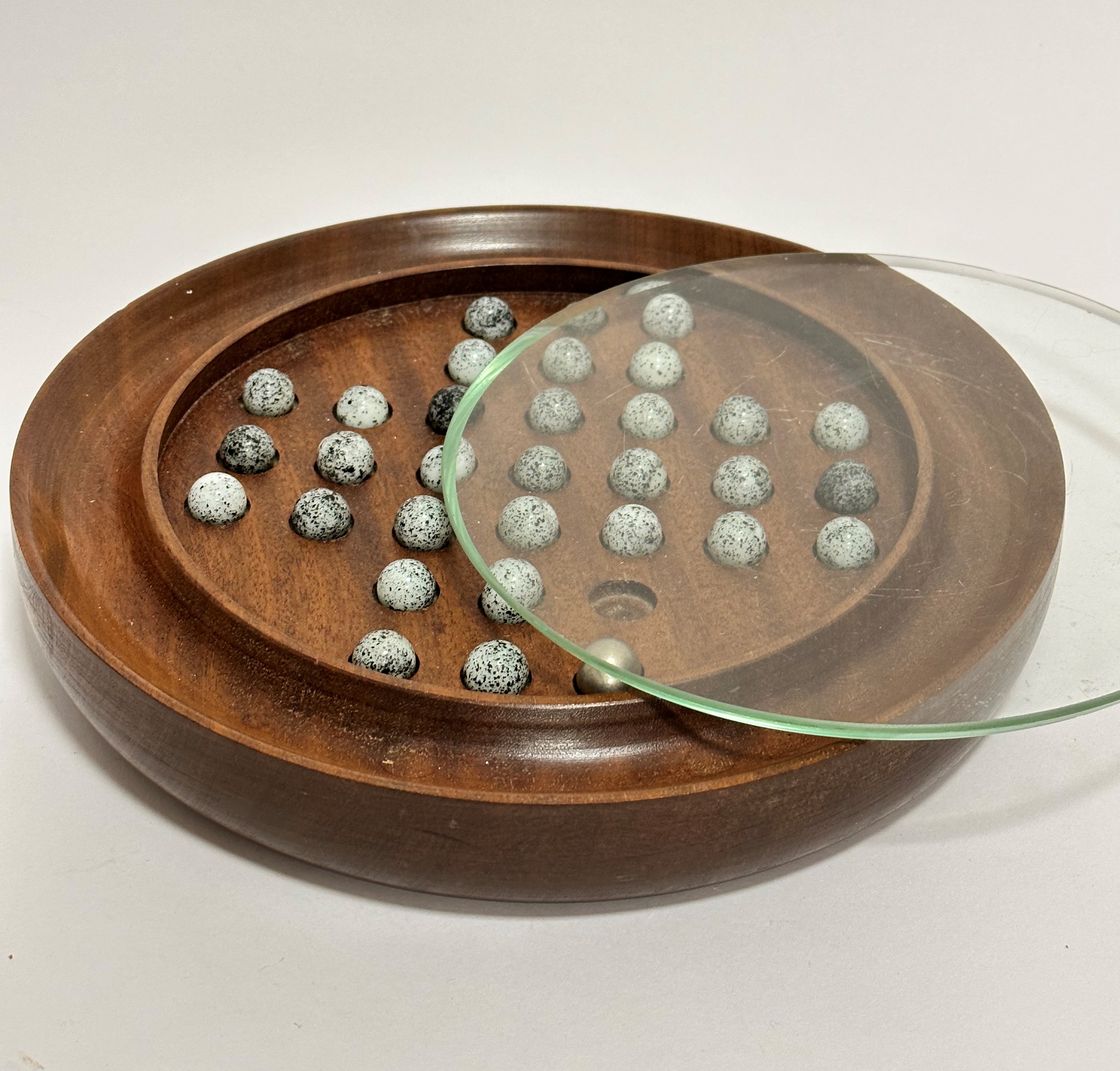 A mahogany circular shaped solitaire game including thirty-one variegated marble balls with steel