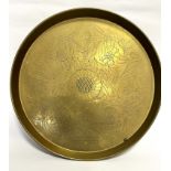 An Eastern inspired circular brass tray with centre flowerhead enclosed within a scrolling leaf