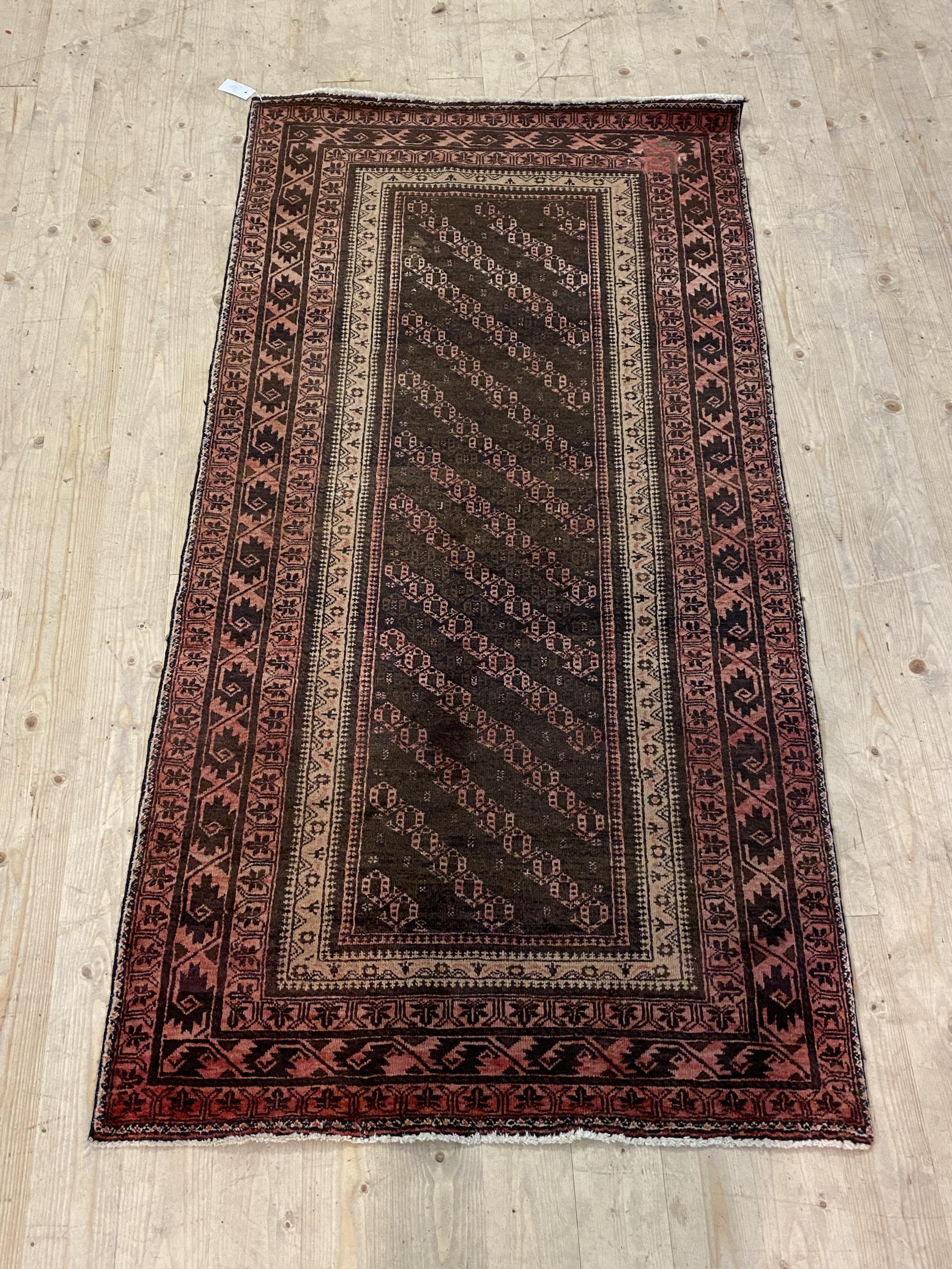 A Persian hand knotted rug, the brown field enclosed by a multi line border 191cm x 99cm