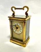 An Edwardian French four glass brass clock with enamelled dial and Roman numerals, with fold down