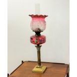 A Victorian corinthian brass cast fluted column oil lamp with cranberry glass overpainted and