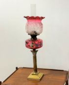 A Victorian corinthian brass cast fluted column oil lamp with cranberry glass overpainted and