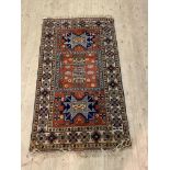 A Caucasian hand knotted rug, the red field with stylised geometric design and bordered 106cm x