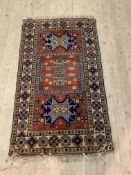 A Caucasian hand knotted rug, the red field with stylised geometric design and bordered 106cm x