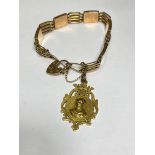 A 9ct gold gatelink bracelet suspending a 15ct gold shield-form fob, the bracelet spaced by engraved