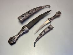 Two Middle-Eastern damascened white metal jambiya daggers, each with curved blade, the grips and