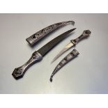 Two Middle-Eastern damascened white metal jambiya daggers, each with curved blade, the grips and