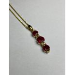 A 14ct yellow gold ruby and diamond pendant, the three graduated round-cut rubies claw set on a